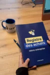 Registre des achats micro-entreprise LA MICRO BY FLO sur un bureau avec mug et stylo